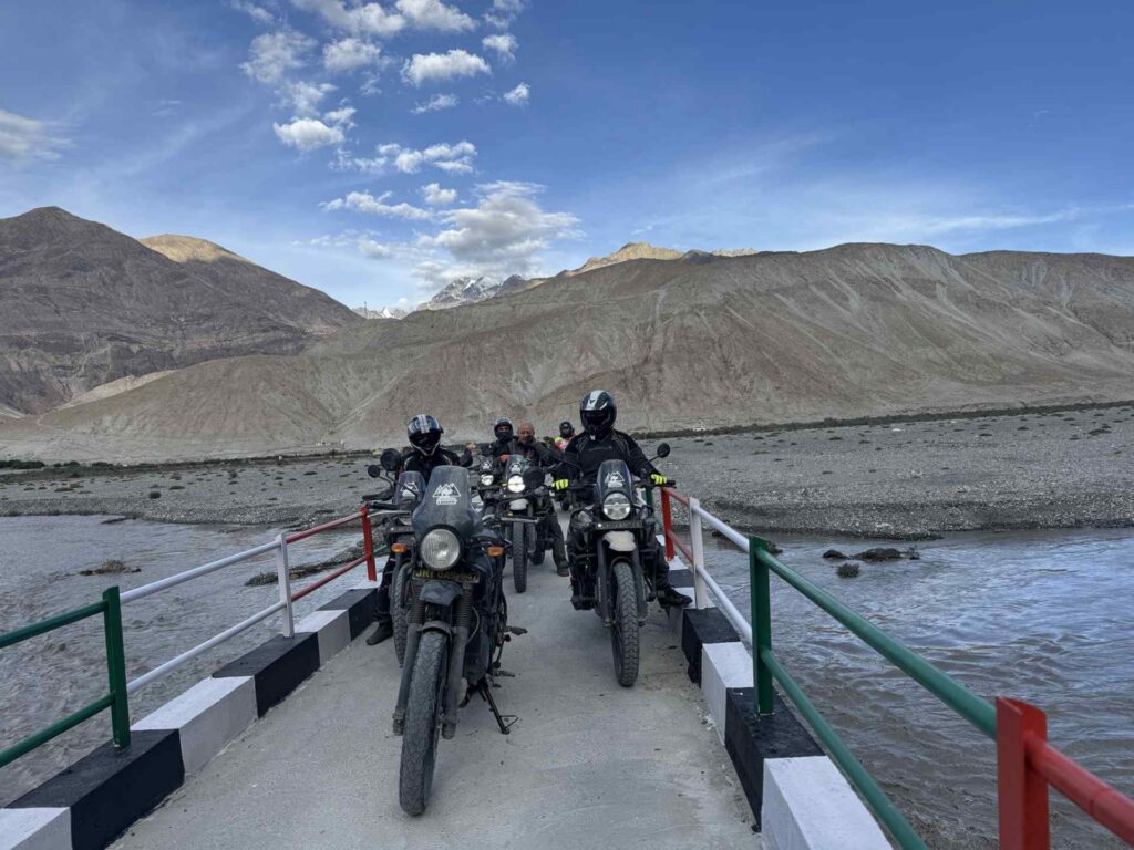 Riders on Royal Enfield Himalayan motorcycles crossing a bridge in the Ladakh Himalayas