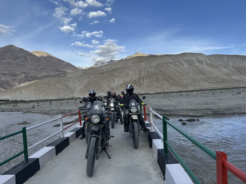 Riders on Royal Enfield Himalayan motorcycles crossing a bridge in the Ladakh Himalayas