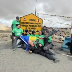 Riders and the Leh ground crew in matching green shirts at the Umling La sign (5,798 m), Ladakh